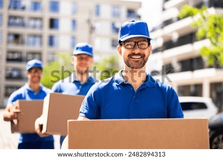 Professional Delivery Men Efficiently Transporting Cardboard Boxes in Front of Company Truck on Sunny Day
