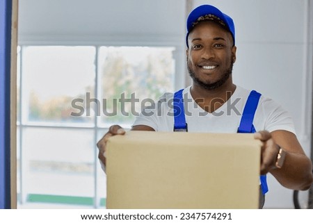 Professional delivery service employee of a man in a blue cap qualitatively and quickly performs his work. Smiling young black guy delivers parcel in blue uniform in cardboard box to customer's house. Stock foto © 
