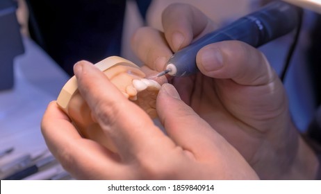 Professional dental technician or dentist holding motor handpiece tool and working with dental prosthesis, tooth dentures - close up view. Stomatology, medicine, restoration concept