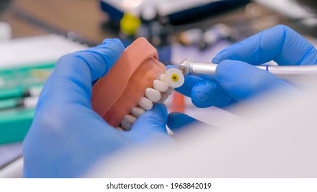 Professional dental technician or dentist holding motor handpiece tool and working with dental prosthesis, tooth dentures - close up view. Stomatology, medicine, restoration concept