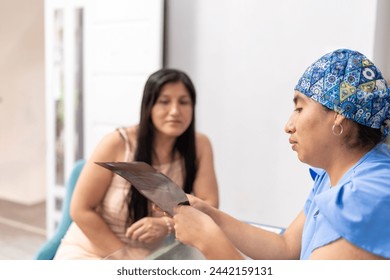 A professional dentist in a patterned scrub cap examines a dental X-ray with her attentive patient - Powered by Shutterstock