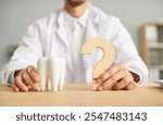 Professional dentist ready to answer all your questions about teeth health. Closeup male hands holding a white tooth model and a wooden question mark on the table. Dental care, stomatology concept