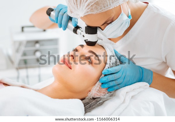 Professional dermatology.\
Pleasant young woman having her skin checked while visiting a\
dermatology clinic