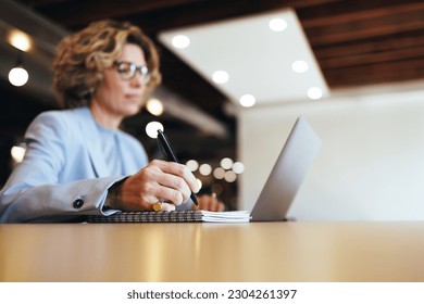 Professional designer creating a to do list on a notepad at work. Business woman writing in her diary in a coworking office. Mature business woman sitting at a desk with a laptop.