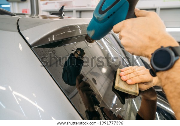 Professional detailer warms up\
tint film with industrial dryer to apply tinting on car glass,\
close up