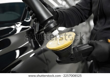 Professional detailing of the car in the auto studio, the master applies paste or wax to the car body polishing machine