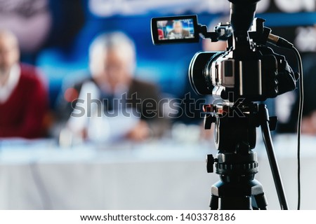 Professional digital camera recording presentation of a blurred speaker wearing suit, live streaming concept