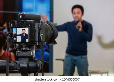 Professional Digital Mirrorless Camera With Microphone On The Tripod Recording Video Blog Of Asian Speaker On The Stage Seminar, Camera For Photographer Or Video And Technology Live Streaming Concept