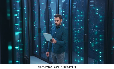 IT professional with digital tablet monitoring system performance of database network servers working on rack in high tech data center. Webhosting, cloud computing.