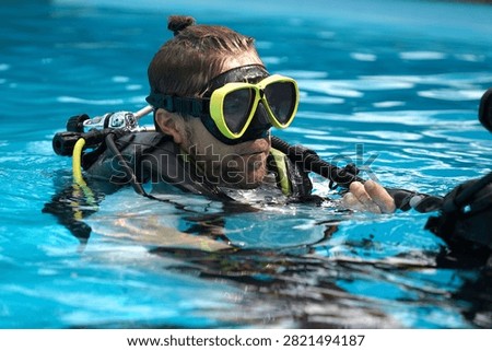 A professional diver and a novice practice diving in a pool.