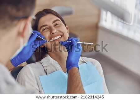 Professional doctor is checking woman's teeth in light modern dental clinic