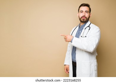 Professional Doctor With A Lab Coat Pointing To Copy Space Against A Yellow Background