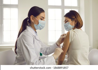 Professional doctor or nurse giving flu or COVID-19 injection to patient. Woman in medical face mask getting antiviral vaccine at hospital or health center during vaccination and immunization campaign - Powered by Shutterstock