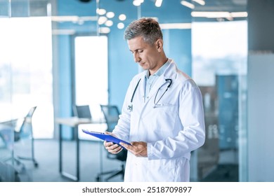 A professional doctor wearing a white coat and stethoscope reviews patient records on a clipboard in a modern hospital. - Powered by Shutterstock