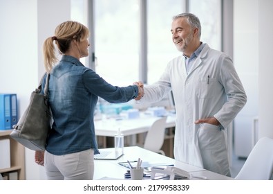 Professional doctor welcoming a patient in his office, the are smiling and shaking hands - Powered by Shutterstock