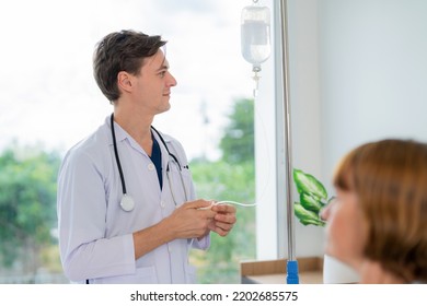 Professional Doctor In The White Coat Put A Stethoscope Around Neck Adjust The Speed Of Saline Solution To Elderly Woman Who Lying Down On The Bed At Nursing Home. Visit Patient At Ward In
Hospital