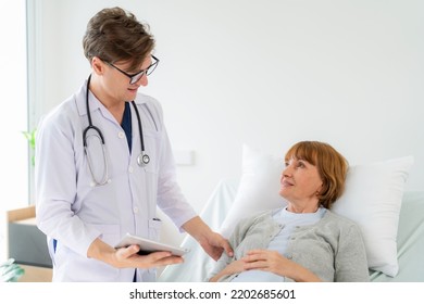 Professional Doctor In The White Coat Put A Stethoscope Around Neck Holding Tablet And Talked To
Elderly Woman Who Lying Down On The Bed At Nursing Home. Caregivers Provide Care Medical Service.