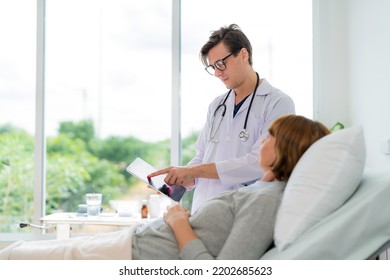 Professional Doctor In The White Coat Put A Stethoscope Around Neck Holding Tablet And Talked To
Elderly Woman Who Lying Down On The Bed At Nursing Home. Caregivers Provide Care Medical Service.