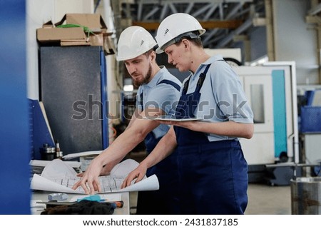 Professional drafter working in factory showing technical drawing to his female coworker, medium shot