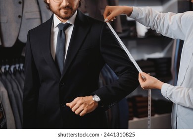 Professional dressmaker taking measurements of businessman in atelier classic menswear. Tailor fitting bespoke suit to handsome man. - Powered by Shutterstock