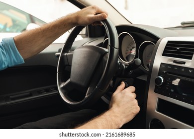 Professional Driver Concept. Closeup of man putting car key to the keyhole, starting the car or stopping engine sitting on driver's seat. Guy holding hands on steering wheel, over the shoulder view