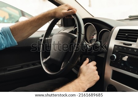 Professional Driver Concept. Closeup of man putting car key to the keyhole, starting the car or stopping engine sitting on driver's seat. Guy holding hands on steering wheel, over the shoulder view
