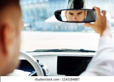 Professional driving. Confident smart man looking into the rearview mirror while driving his car