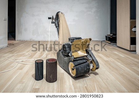 Professional drum floor sander machine and sanding belts on wooden floor. Industrial theme