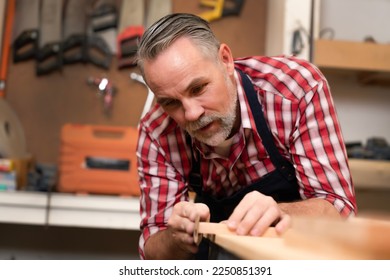 Professional elder carpenter using sandpaper to clean wood after cutting, making wood smooth without splintering before assembly furniture. Senior joiner skill focuses a perfectionist of woodcraft.