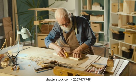 Professional Elderly Man Carpenter Working On Wood Using Carpentry Tools In The Garage. Craft Authentic Workshop. Handicraft, Creative Small Business. Profession, Art And Hobby Concept.