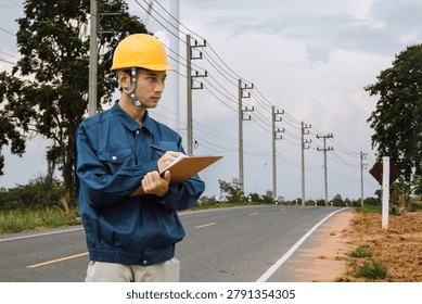 Professional electrical engineer inspecting roadside power line infrastructure with clipboard, representing utility maintenance, energy distribution and electrical engineering work.