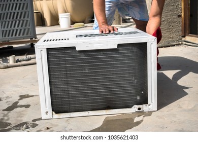 a professional electrician is cleaning the window air conditioner on the roof top of a house with a wet napkin 