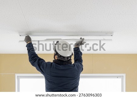 Professional Electrician Installing LED Base Light Fixture on Office Ceiling - Commercial Renovation, Electrical Maintenance and Facility Management Concept