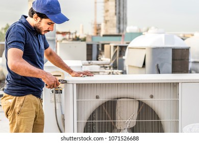 a professional electrician man is fixing the heavy unit of an air conditioner at the roof top of a building and wearing blue uniform and head cap - Shutterstock ID 1071526688