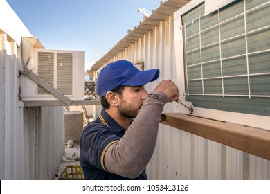 a professional electrician man is fixing the window unit of an air conditioner at the roof top of a building and wearing blue uniform and head cap