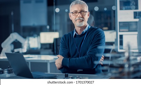 Professional Electronics Design Engineer Wearing Glasses Works on Laptop Computer in Research Laboratory. In the Background Motherboards, Circuit Board, Heavy Industry Robotic Components - Powered by Shutterstock