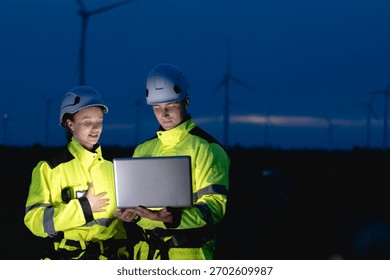 Professional engineer team working at night shift. Workers teamwork in wind turbine field. Technician technology expert work with safety dress survey inspecting outdoor.