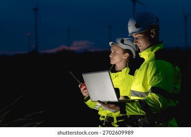 Professional engineer team working at night shift. Workers teamwork in wind turbine field. Technician technology expert work with safety dress survey inspecting outdoor.