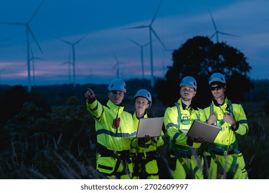 Professional engineer team working at night shift. Workers teamwork in wind turbine field. Technician technology expert work with safety dress survey inspecting outdoor.