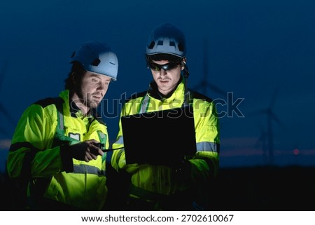 Professional engineer team working at night shift. Workers teamwork in wind turbine field. Technician technology expert work with safety dress survey inspecting outdoor.