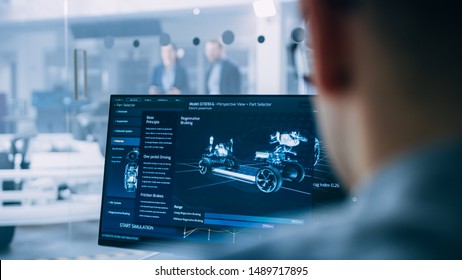 Professional Engineer Works On A Computer With A 3D CAD Software And Tests The Electric Car Chassis Prototype With Wheels, Batteries And Engine Standing In A High Tech Development Laboratory.