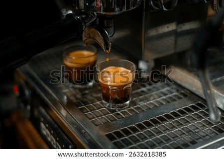 professional espresso machine in action, simultaneously brewing two shots of rich, dark espresso into small clear glasses. The golden-brown crema is visible on top of each shot