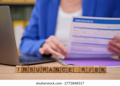 A professional examines an insurance document while sitting at a desk. Scrabble-like tiles spell out insurance risk, highlighting the importance of careful evaluation in this field
