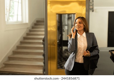 A professional exits a sleek elevator, engaged in a lively mobile discussion.