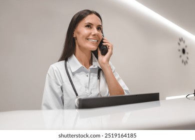 A professional and experienced Caucasian female doctor is talking on the phone with her patient while working in her hospital office, telling healthcare checkup test results, bringing good news - Powered by Shutterstock