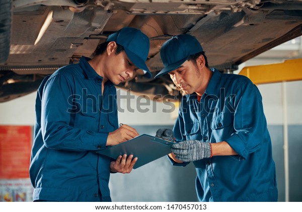 Professional experienced Vietnamese\
mechanics checking list of car problems after inspecting\
it