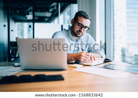 Professional expert working with information for business report about corporate money investment writing notes in textbook during time for online researching on laptop computer,digital marketing