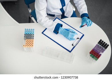 Professional Facility Research In Healthcare System. Top View Of Female Laboratory Worker Making Notes While Studying Blood Samples In Lab Office