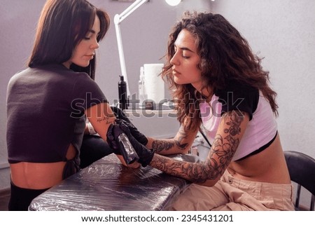 Professional female artist creating custom lettering tattoo on arm of woman