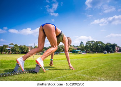 Professional Female Athlete Start On Green Grass Under Blue Sky. Track And Field, Running, Athletics Sport Photo.